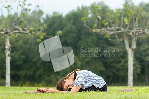 Image of Young beautiful woman doing yoga exercise in green park. Healthy lifestyle and fitness concept.