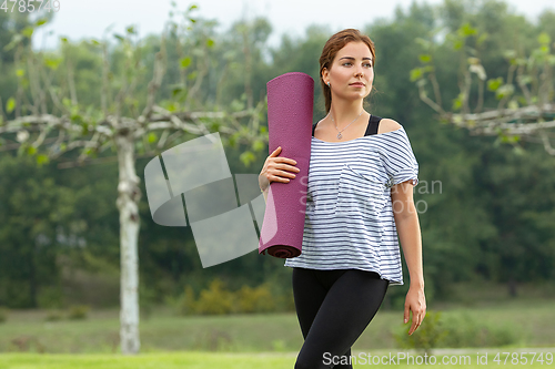 Image of Young beautiful woman doing yoga exercise in green park. Healthy lifestyle and fitness concept.