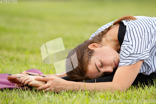 Image of Young beautiful woman doing yoga exercise in green park. Healthy lifestyle and fitness concept.