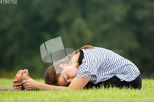 Image of Young beautiful woman doing yoga exercise in green park. Healthy lifestyle and fitness concept.