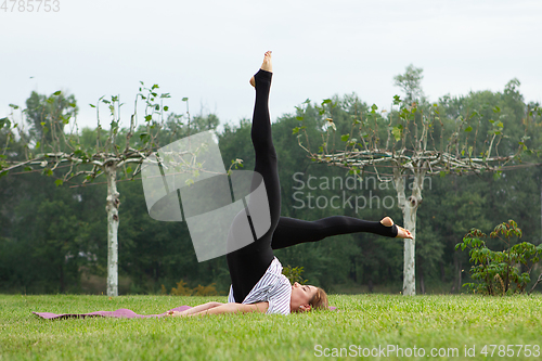 Image of Young beautiful woman doing yoga exercise in green park. Healthy lifestyle and fitness concept.