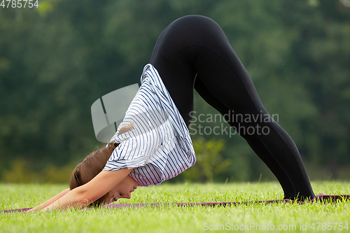 Image of Young beautiful woman doing yoga exercise in green park. Healthy lifestyle and fitness concept.