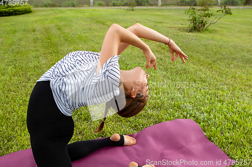 Image of Young beautiful woman doing yoga exercise in green park. Healthy lifestyle and fitness concept.