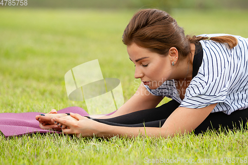 Image of Young beautiful woman doing yoga exercise in green park. Healthy lifestyle and fitness concept.