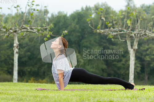 Image of Young beautiful woman doing yoga exercise in green park. Healthy lifestyle and fitness concept.