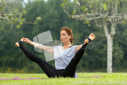 Image of Young beautiful woman doing yoga exercise in green park. Healthy lifestyle and fitness concept.