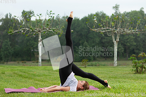 Image of Young beautiful woman doing yoga exercise in green park. Healthy lifestyle and fitness concept.