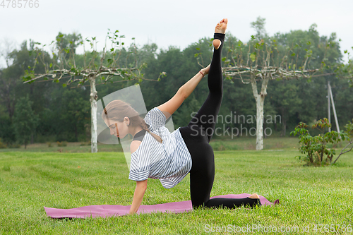 Image of Young beautiful woman doing yoga exercise in green park. Healthy lifestyle and fitness concept.