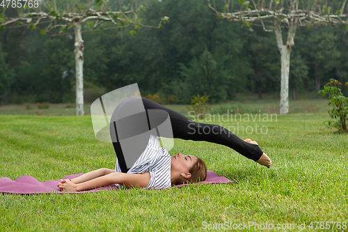 Image of Young beautiful woman doing yoga exercise in green park. Healthy lifestyle and fitness concept.