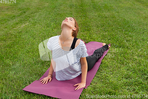 Image of Young beautiful woman doing yoga exercise in green park. Healthy lifestyle and fitness concept.