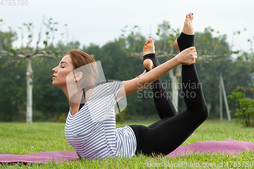 Image of Young beautiful woman doing yoga exercise in green park. Healthy lifestyle and fitness concept.