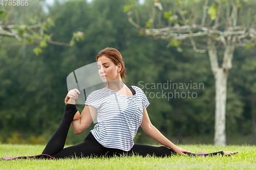 Image of Young beautiful woman doing yoga exercise in green park. Healthy lifestyle and fitness concept.