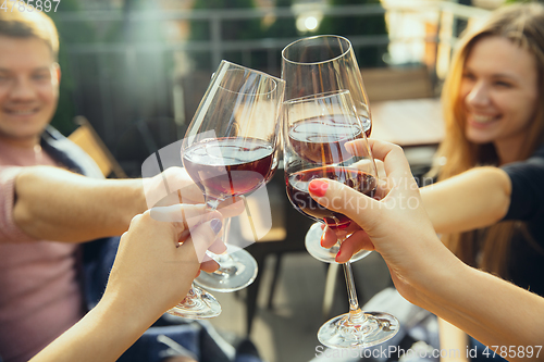 Image of People clinking glasses with wine on the summer terrace of cafe or restaurant. Close up shot, lifestyle.