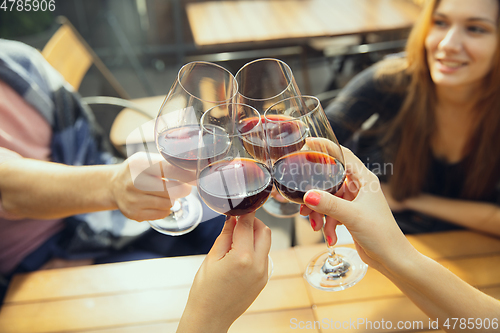 Image of People clinking glasses with wine on the summer terrace of cafe or restaurant. Close up shot, lifestyle.