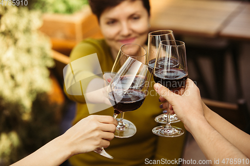 Image of People clinking glasses with wine on the summer terrace of cafe or restaurant. Close up shot, lifestyle.