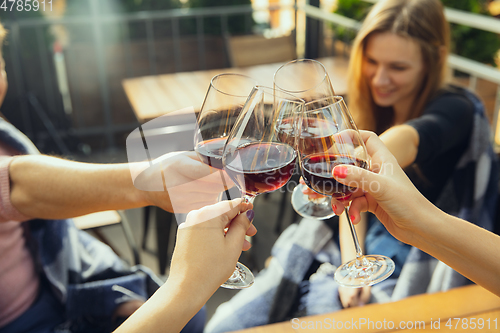 Image of People clinking glasses with wine on the summer terrace of cafe or restaurant. Close up shot, lifestyle.