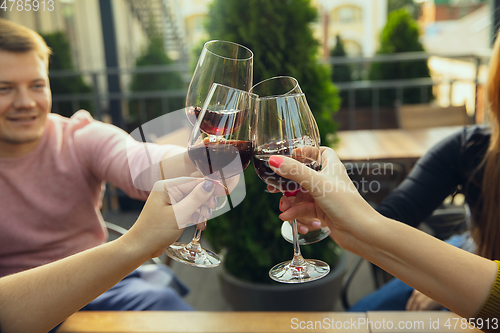 Image of People clinking glasses with wine on the summer terrace of cafe or restaurant. Close up shot, lifestyle.