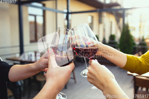 Image of People clinking glasses with wine on the summer terrace of cafe or restaurant. Close up shot, lifestyle.