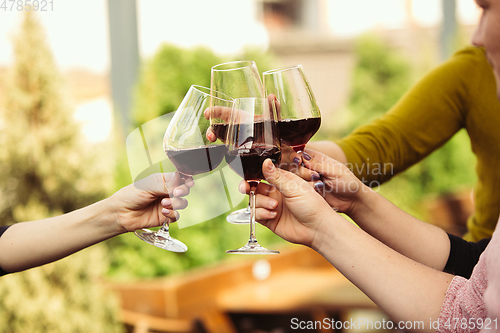 Image of People clinking glasses with wine on the summer terrace of cafe or restaurant. Close up shot, lifestyle.