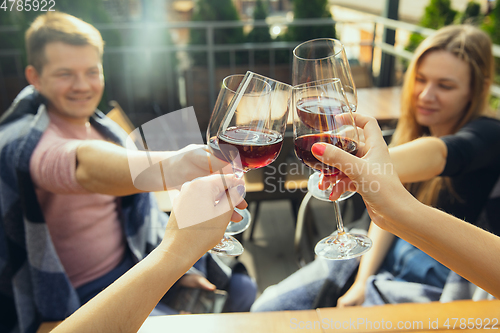 Image of People clinking glasses with wine on the summer terrace of cafe or restaurant. Close up shot, lifestyle.