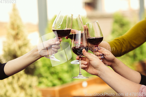 Image of People clinking glasses with wine on the summer terrace of cafe or restaurant. Close up shot, lifestyle.