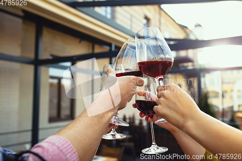 Image of People clinking glasses with wine on the summer terrace of cafe or restaurant. Close up shot, lifestyle.