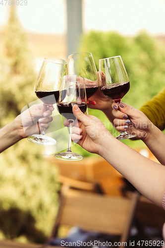 Image of People clinking glasses with wine on the summer terrace of cafe or restaurant. Close up shot, lifestyle.