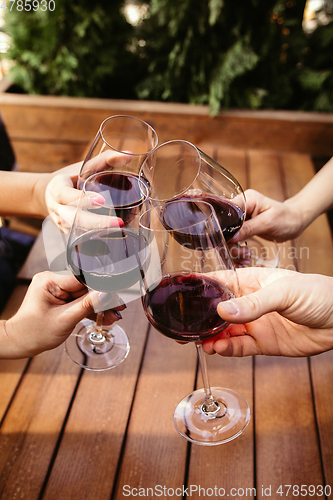 Image of People clinking glasses with wine on the summer terrace of cafe or restaurant. Close up shot, lifestyle.