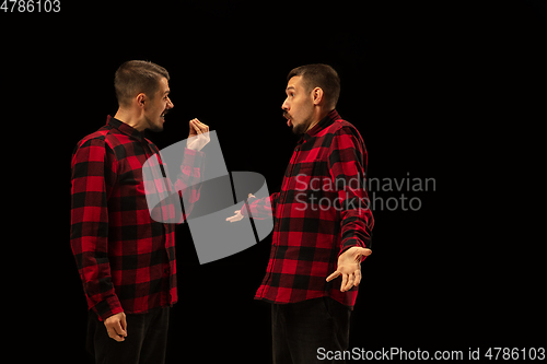 Image of Young handsome man arguing with himself on black studio background.