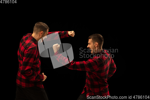 Image of Young handsome man arguing with himself on black studio background.