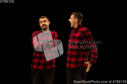 Image of Young handsome man arguing with himself on black studio background.