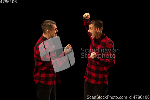 Image of Young handsome man arguing with himself on black studio background.