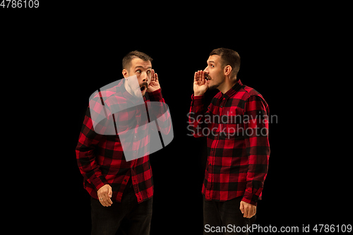 Image of Young handsome man arguing with himself on black studio background.