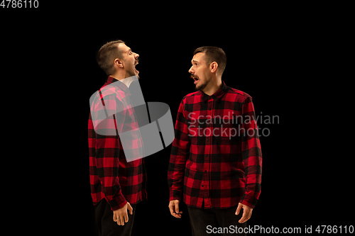 Image of Young handsome man arguing with himself on black studio background.