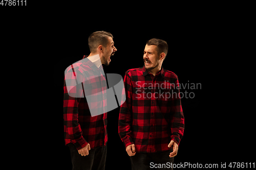 Image of Young handsome man arguing with himself on black studio background.