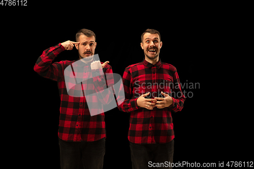 Image of Young handsome man arguing with himself on black studio background.