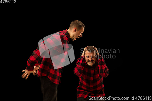 Image of Young handsome man arguing with himself on black studio background.