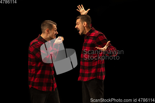 Image of Young handsome man arguing with himself on black studio background.