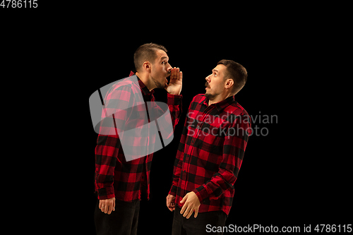 Image of Young handsome man arguing with himself on black studio background.