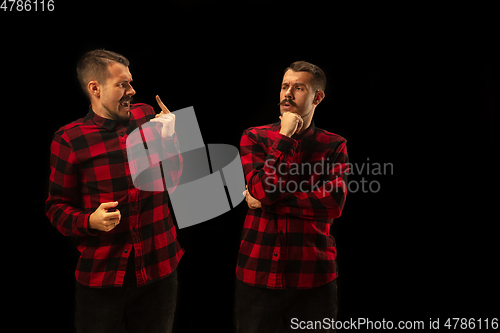 Image of Young handsome man arguing with himself on black studio background.