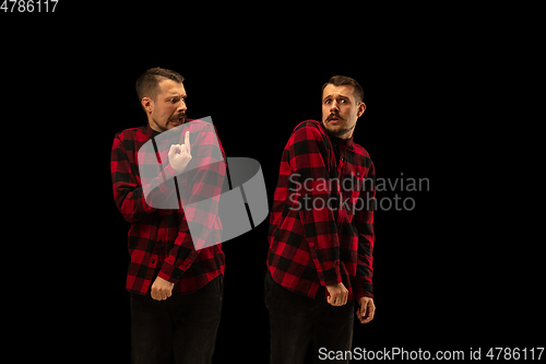 Image of Young handsome man arguing with himself on black studio background.