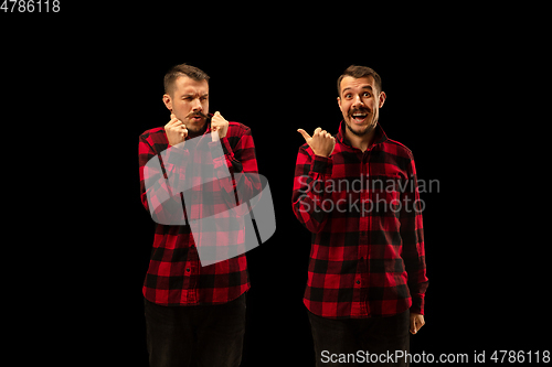 Image of Young handsome man arguing with himself on black studio background.