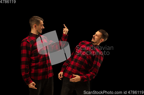 Image of Young handsome man arguing with himself on black studio background.