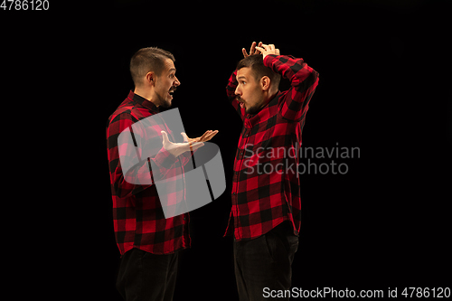 Image of Young handsome man arguing with himself on black studio background.