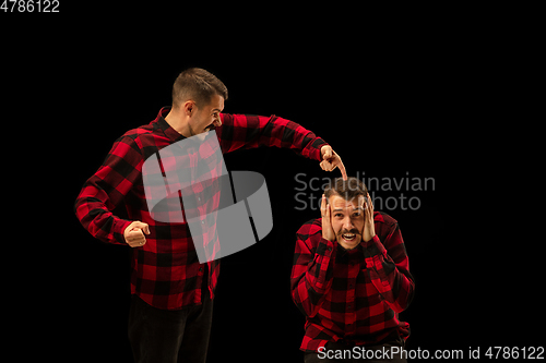 Image of Young handsome man arguing with himself on black studio background.