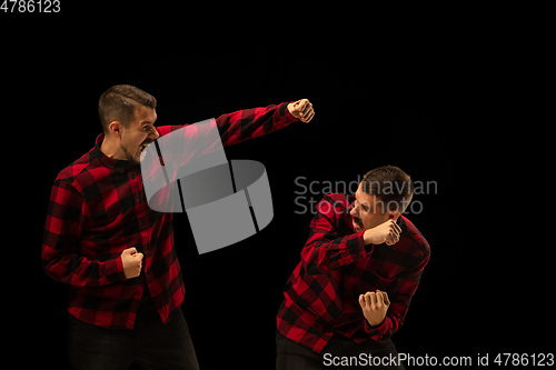 Image of Young handsome man arguing with himself on black studio background.