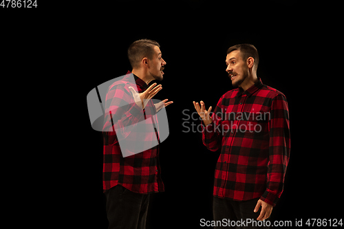 Image of Young handsome man arguing with himself on black studio background.