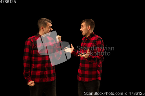 Image of Young handsome man arguing with himself on black studio background.