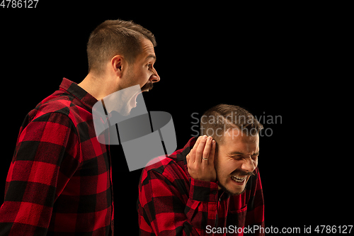 Image of Young handsome man arguing with himself on black studio background.