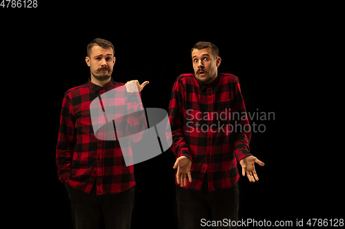 Image of Young handsome man arguing with himself on black studio background.